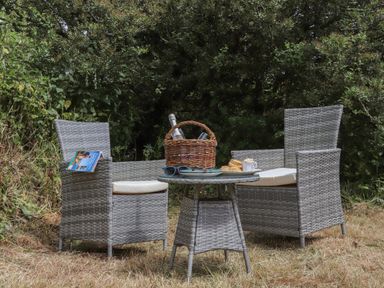 An outdoor seating area with two wicker chairs and a small round table with a basket and food on the table at The Hayloft in Helston