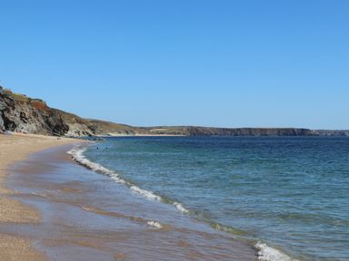 A sandy beach with small waves and cliffs in the background at The Hayloft in Helston