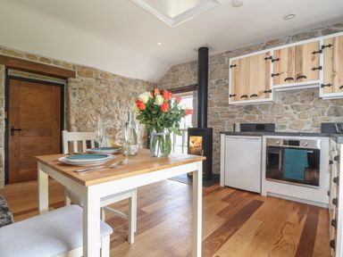 A kitchen and dining area with a wooden table set for two and stone walls at The Hayloft in Helston