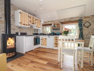 A kitchen with stone walls a wood burning stove wooden cabinets and a dining table with chairs at The Hayloft in Helston