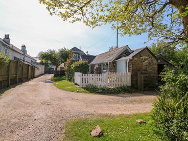 A gravel driveway leading to stone and white cottages with a white picket fence and greenery at Toad Hall Cottage Hutcherleigh near Blackawton