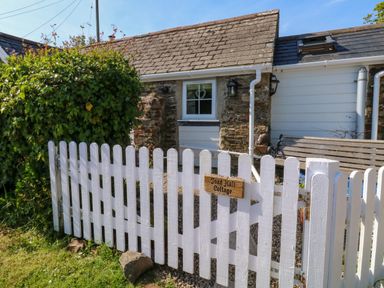 A white picket fence with a wooden sign in front of a small stone cottage at Toad Hall Cottage Hutcherleigh near Blackawton