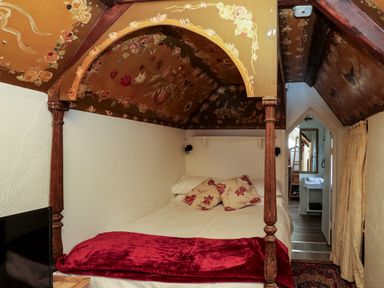 A bedroom with a canopy bed with floral designs on the ceiling and red pillows at Toad Hall Cottage Hutcherleigh near Blackawton