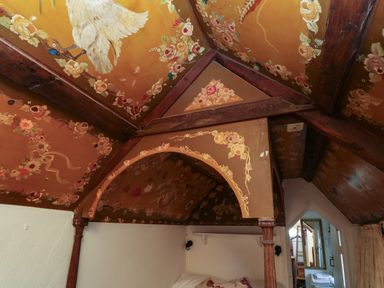 An attic bedroom with a wooden canopy bed and decorative floral and bird paintings on the ceiling at Toad Hall Cottage in Hutcherleigh near Blackawton