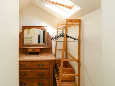 A small room with a wooden dresser with mirror and a wooden clothing rack with hangers at Toad Hall Cottage Hutcherleigh near Blackawton