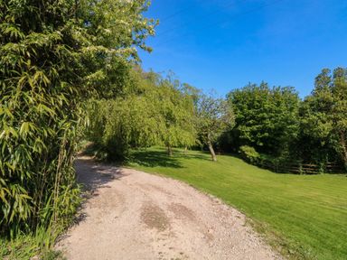 A gravel pathway curving through a grassy area with trees and bushes at Toad Hall Cottage in Hutcherleigh near Blackawton