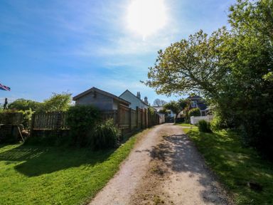 A dirt path leading to houses with wooden fences and trees on both sides with a blue sky above at Toad Hall Cottage in Hutcherleigh near Blackawton