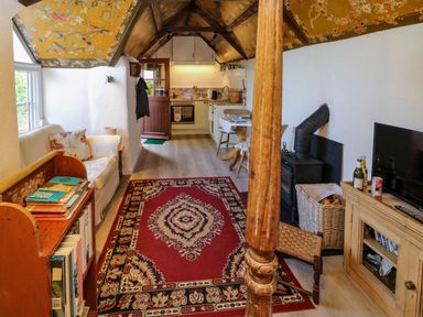 A living room with a bookshelf and floral wallpaper on the ceiling at Toad Hall Cottage Hutcherleigh near Blackawton