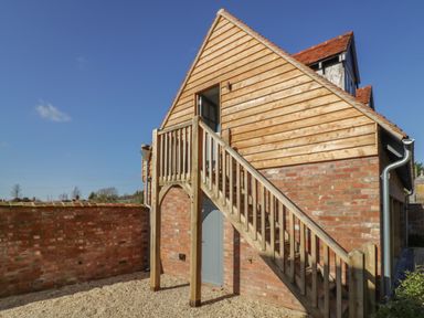 A building with wooden stairs leading to an upper floor and a brick wall surrounding the area at Coach House Mews in Alderminster