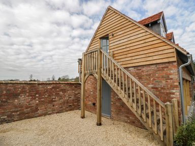 An exterior view of a brick building with wooden cladding and an outdoor wooden staircase at Coach House Mews in Alderminster