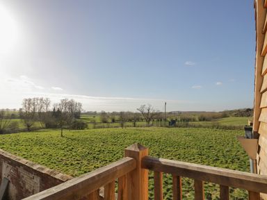 A view of green fields with trees and a wooden railing in the foreground at Coach House Mews in Alderminster