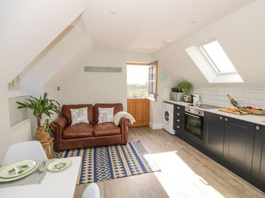 A kitchen with black cabinets a brown leather sofa and a wooden door at Coach House Mews in Alderminster