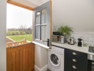 A kitchen area with a half wooden door open to a green field a washing machine microwave toaster coffee machine and a plant on the counter at Coach House Mews in Alderminster