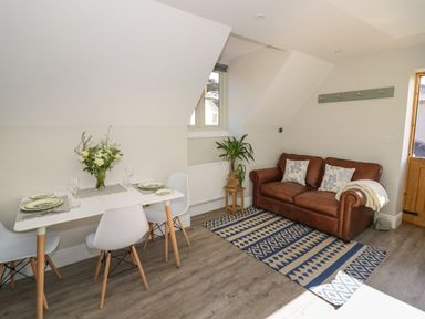 A dining area with a table set for four and a brown sofa with pillows on a patterned rug at Coach House Mews in Alderminster