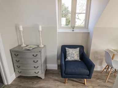 A corner with a blue armchair and a gray chest of drawers with candles at Coach House Mews in Alderminster