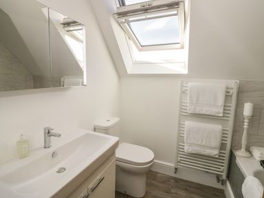 A bathroom with a sink a toilet a towel rack with towels a candle and a skylight window at Coach House Mews in Alderminster