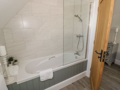 A bathroom with a bathtub shower combination and wooden door at Coach House Mews in Alderminster