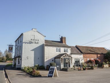 An exterior view of a building named The Bell with a white facade a signboard outside and a paved area in front at Coach House Mews in Alderminster