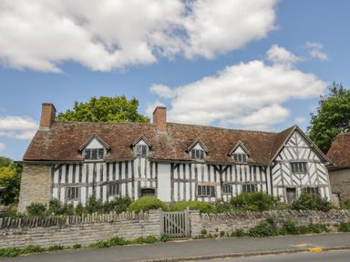 A timber framed house with a tiled roof and a stone wall with a wooden gate