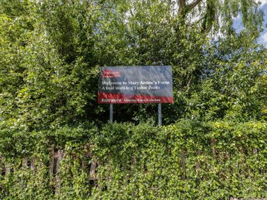 A sign welcoming visitors to Mary Arden's Farm surrounded by green trees and bushes at Coach House Mews in Alderminster