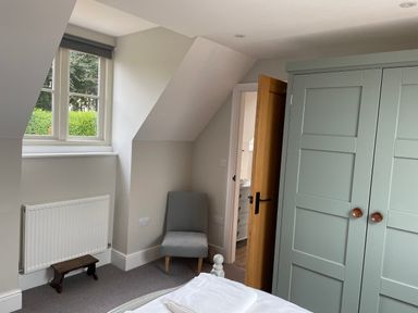 A bedroom with a gray chair a green wardrobe a wooden door and a window at Coach House Mews in Alderminster