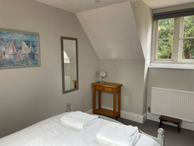 A bedroom with a bed with white linens and towels a small wooden table with a mirror and a window showing trees at Coach House Mews in Alderminster
