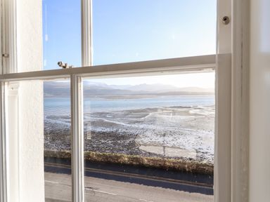 A view of a coastal area with water and mountains seen through a window at Lluest in Beaumaris