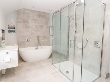 A bathroom with a freestanding bathtub a glass shower enclosure and a wall-mounted sink at Lluest in Beaumaris