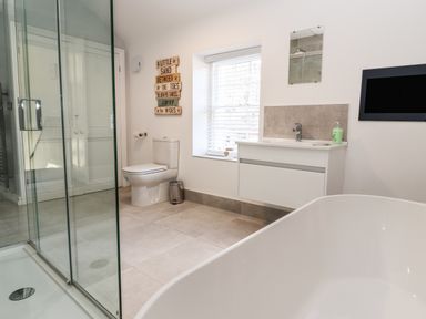 A bathroom with a glass shower enclosure a white toilet a sink with a vanity a bathtub and a window with blinds at Lluest in Beaumaris
