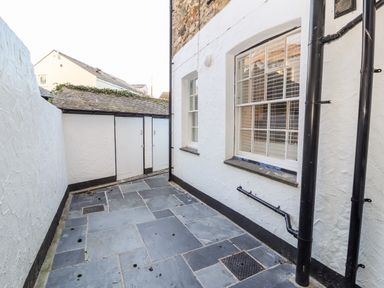An outdoor paved area with white walls black drainage pipes and storage doors at Lluest in Beaumaris
