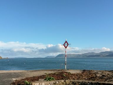 A body of water with a navigational marker and hills in the background at Lluest in Beaumaris