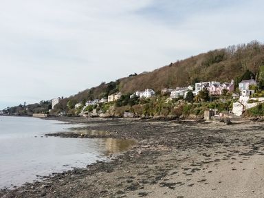 A rocky shoreline with houses on a hillside by the water at Lluest in Beaumaris