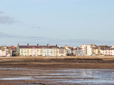 A row of pastel colored buildings along a waterfront with a low tide at Lluest in Beaumaris