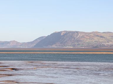 A coastal landscape with tidal mudflats and a mountain range in the distance at Lluest in Beaumaris