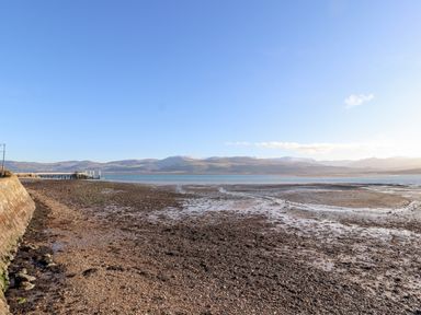 A shoreline with a stone wall and pier overlooking mountains across the water at Lluest in Beaumaris
