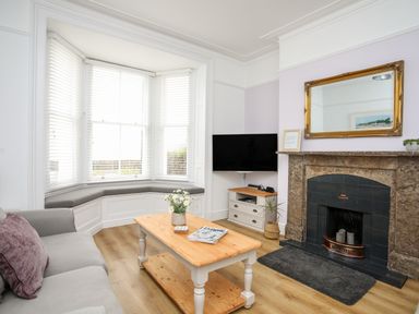 A living room with a grey sofa a wooden coffee table and a fireplace with a mirror above at Lluest in Beaumaris