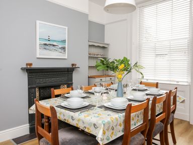 A dining room with a table set for eight people next to a window with blinds and a fireplace at Lluest in Beaumaris