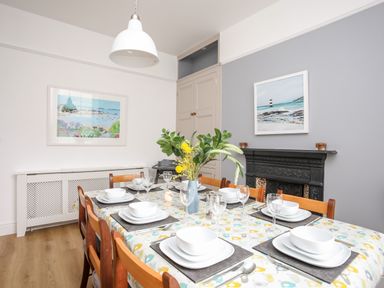 A dining room with a set table and floral centerpiece near a fireplace and framed pictures at Lluest in Beaumaris