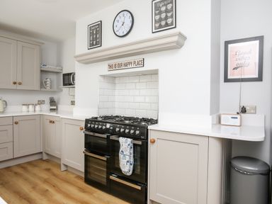A kitchen with a black stove white tiled backsplash cabinets and wooden floor at Lluest in Beaumaris