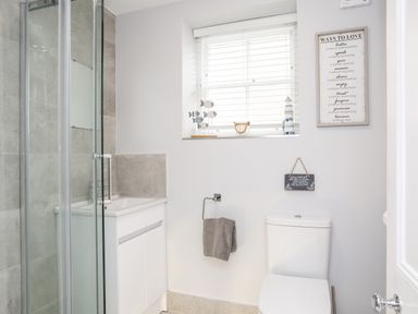 A bathroom with a shower enclosure a sink with cabinet a toilet and a window with blinds at Lluest in Beaumaris