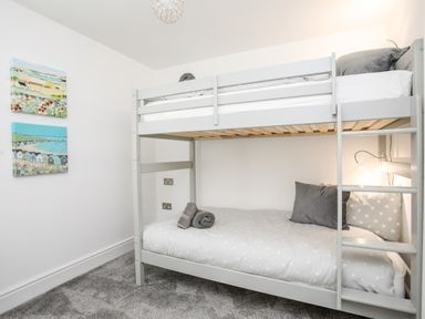 A bedroom with a gray bunk bed gray pillows and rolled towels on the lower bed two paintings on the wall at Lluest in Beaumaris