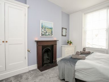 A bedroom with a bed folded towels on it a fireplace a dresser with flowers and a window with blinds at Lluest in Beaumaris