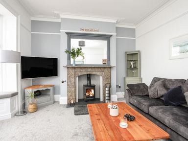 A living room with a fireplace and firewood stove a gray sofa and a wooden coffee table at Lluest in Beaumaris