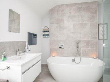 A bathroom with a white freestanding bathtub a white sink with a faucet and a mirror above at Lluest in Beaumaris