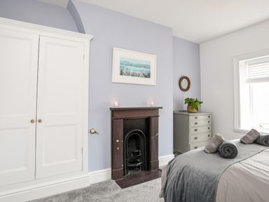 A bedroom with a bed, a fireplace, a wardrobe, a chest of drawers, and a window at Lluest in Beaumaris