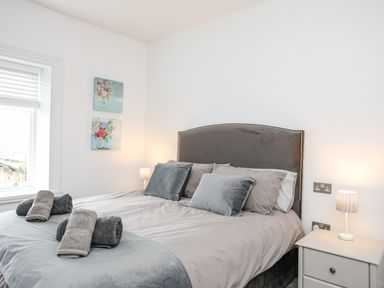 A bedroom with a bed made up with pillows and towels bedside tables with lamps and two paintings on the wall at Lluest in Beaumaris