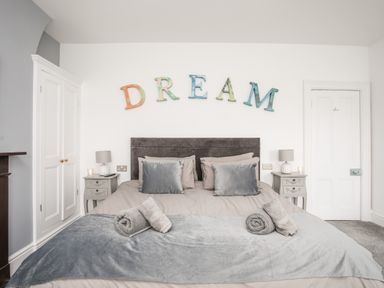A bedroom with a double bed two bedside tables lamps and letters spelling dream on the wall at Lluest in Beaumaris