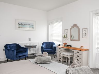 A bedroom with two blue armchairs a small side table and a dressing table with a mirror and stool at Lluest in Beaumaris