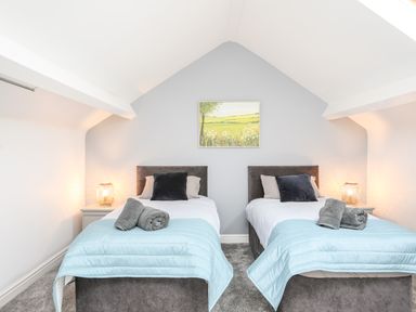 A bedroom with two single beds blue throws and grey towels on each bed a painting above the beds and lamps on side tables at Lluest Beaumaris