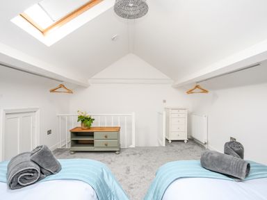 A bedroom with two beds with blue throws and grey towels a skylight a small cabinet and hanging rails at Lluest in Beaumaris